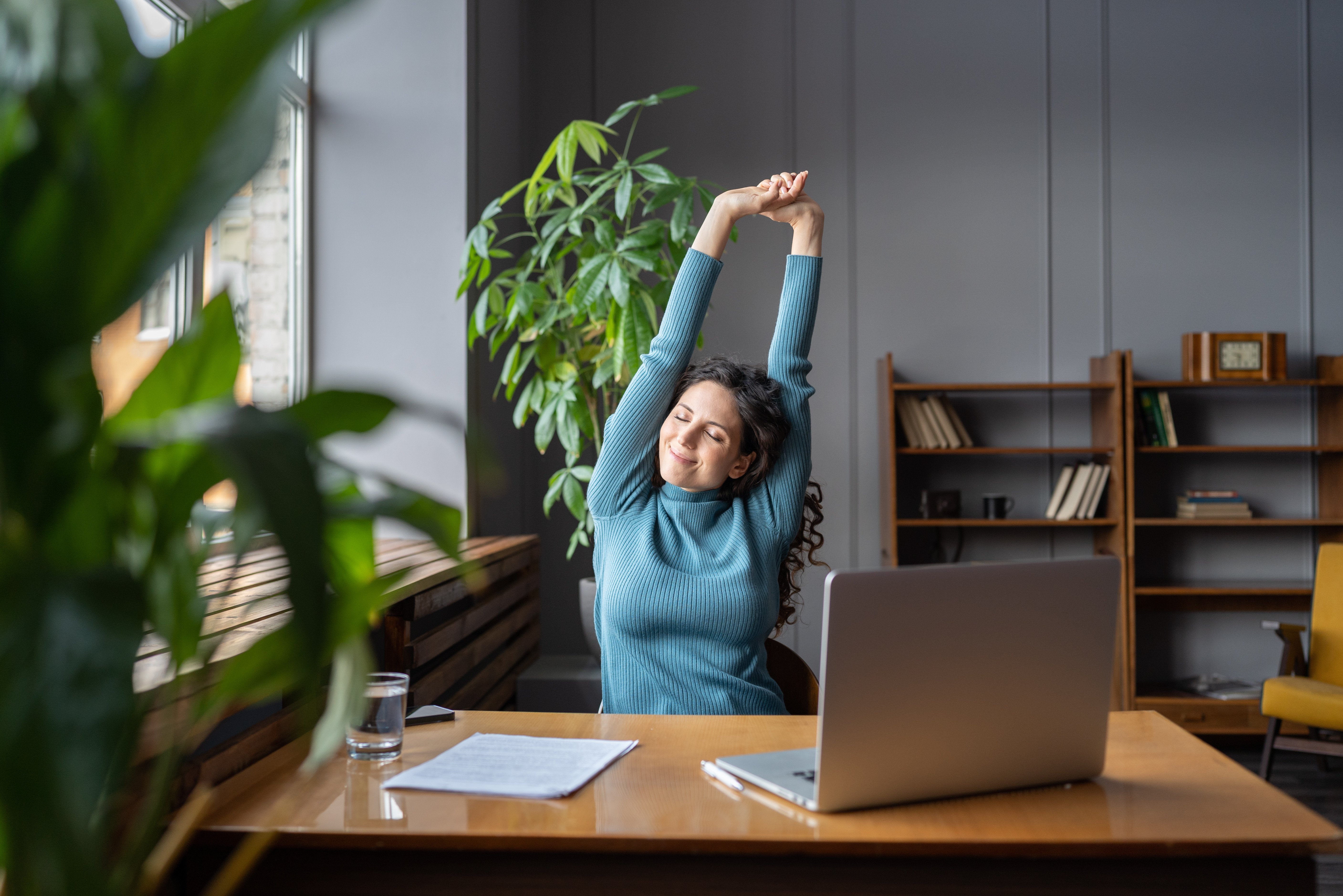 woman sitting behind desk and computer stretching with arms above head