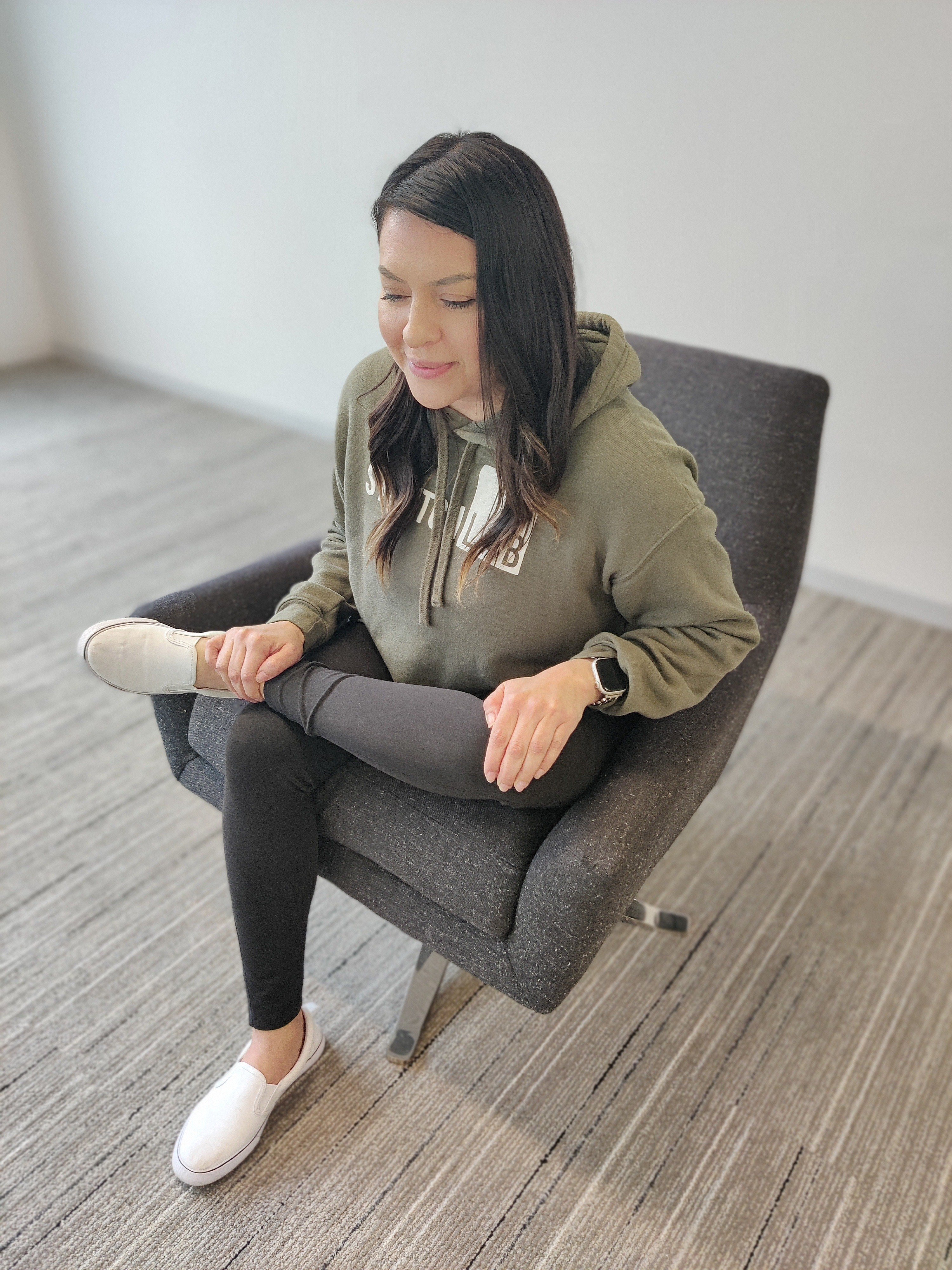 female in green StretchLab sweater doing a seated figure 4 stretch in chair