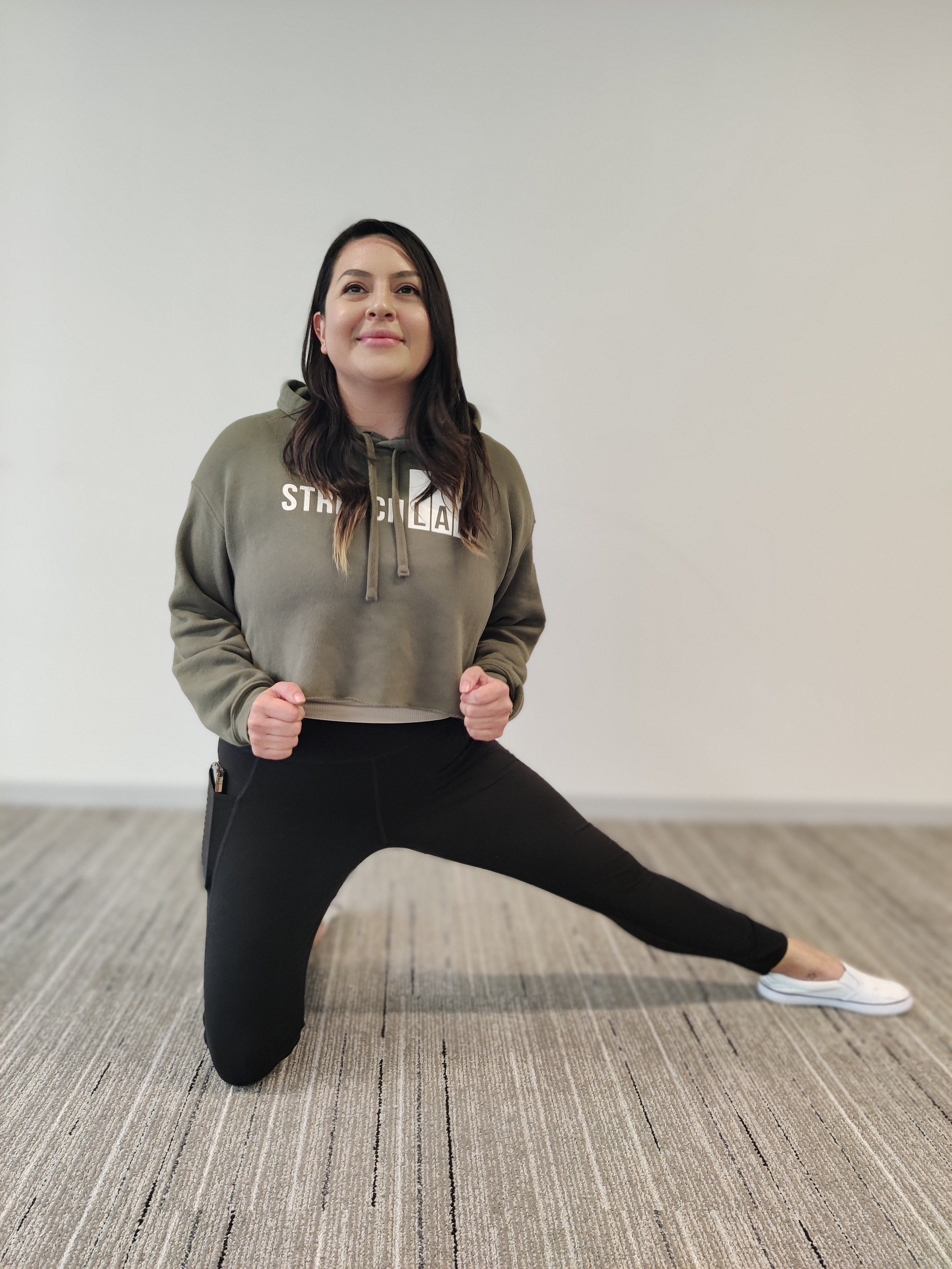 female in green StretchLab sweater doing a kneeling tripod stretch on floor